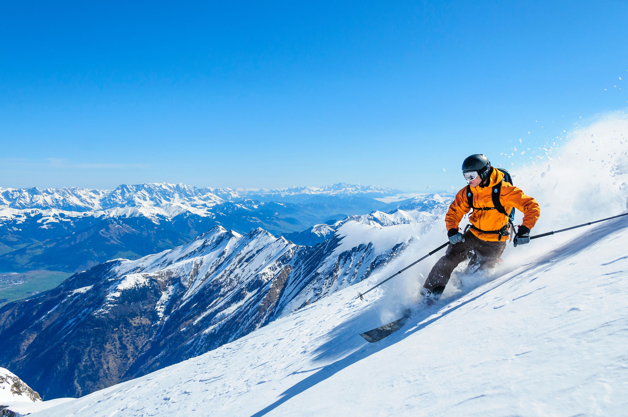 Man in orange coat skiing down mountain in white powdered snow